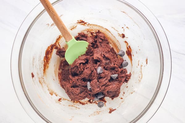 Chocolate cookie dough mixed in a glass bowl with a rubber spatula.