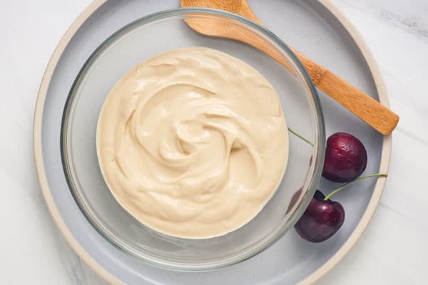 Small bowl of coffee-colored yogurt on a plate with fresh whole cherries.