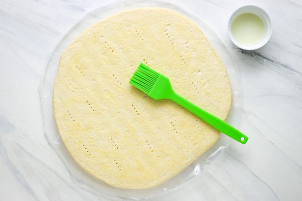 Green pastry brush, ramekin of oil, and frozen pizza crust.
