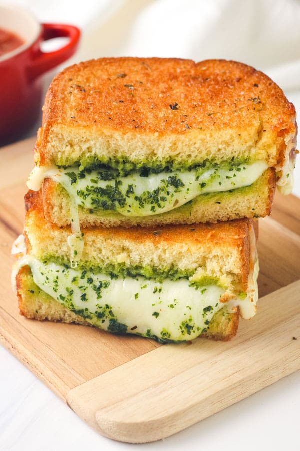 Stacked sandwich slices with pesto and melted cheese oozing out.