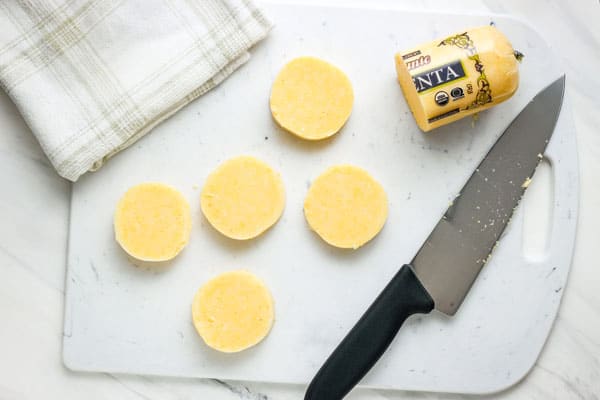 Sliced polenta on a cutting board next to a kitchen towel.
