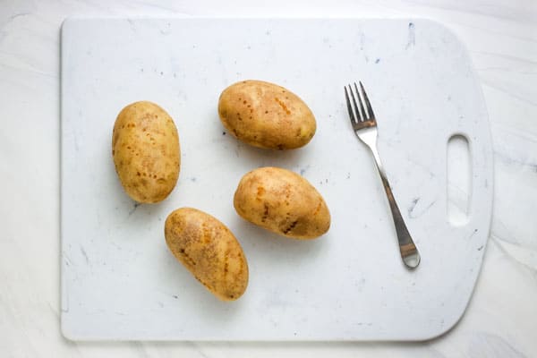 Cutting board with a fork and russet potatoes that have been pricked all over.