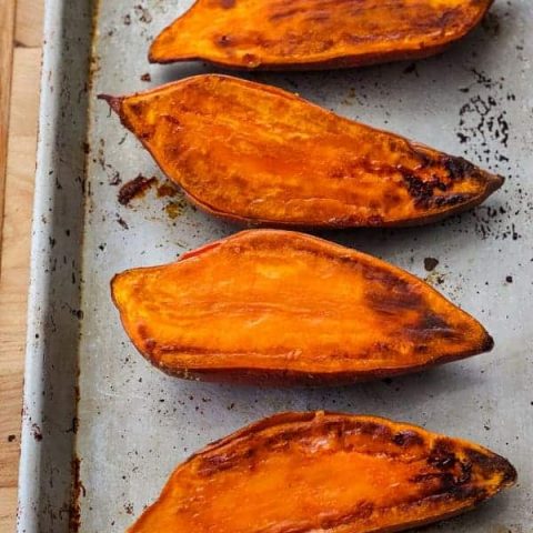 Cooked sweet potato halves on a quarter sheet pan.