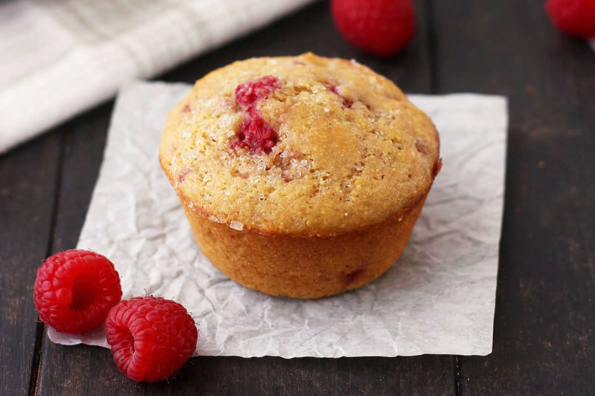 Baked muffin next to fresh raspberries on a table.