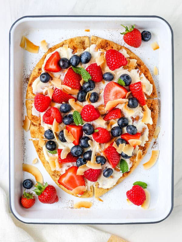 Overhead view of toasted flatbread topped with fresh blueberries, strawberries, raspberries, and coconut chips.
