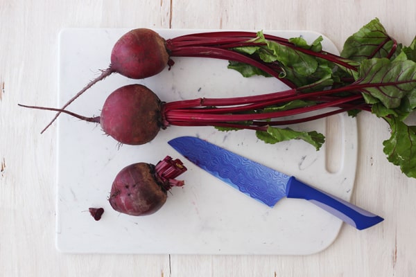 Red beets with leaves attached on a cutting board.