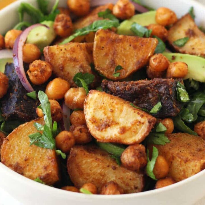 Closeup of roasted chickpeas, potato chunks, and arugula in a white bowl.