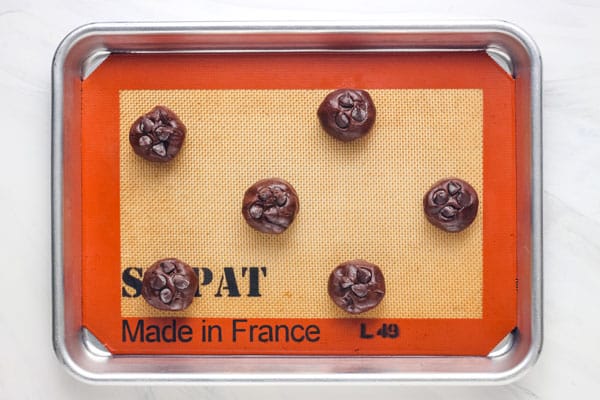 Chocolate dough balls on a small pan lined with a silicone baking mat.