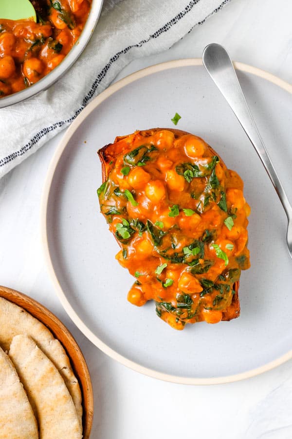 Sweet potato topped with saucy beans next to a plate of pita bread.