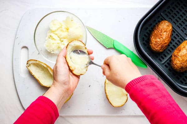 Hands scooping potato middles with a spoon.