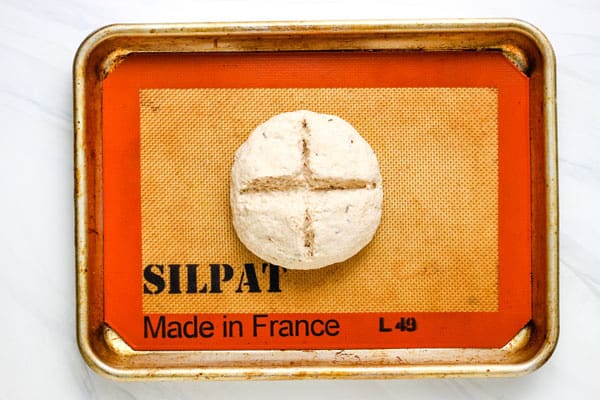 Small dough ball on a pan with a cross sliced across the top.