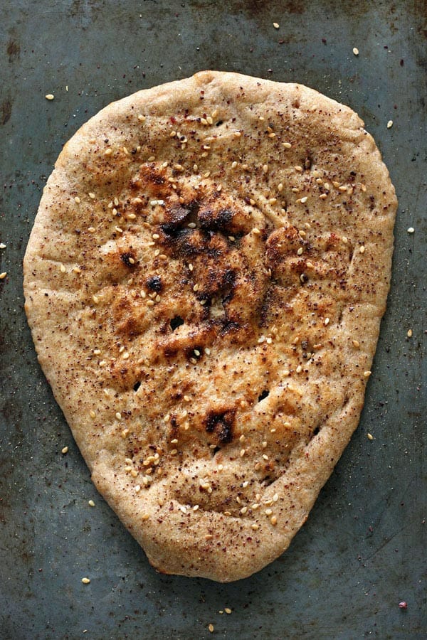 Overhead view of a toasted seasoned flatbread on a baking sheet.