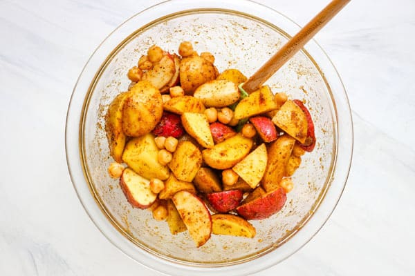 Large glass bowl with seasoned potato chunks and chickpeas.