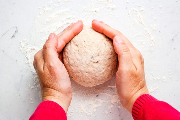 Hands cupped around dough shaping it into a circle.