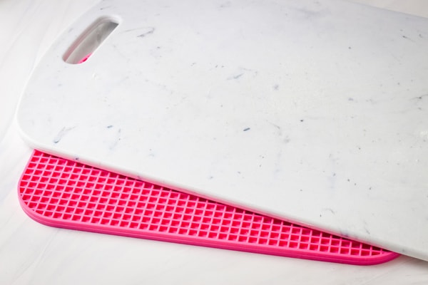 Pink silicone trivet under a plastic cutting board.