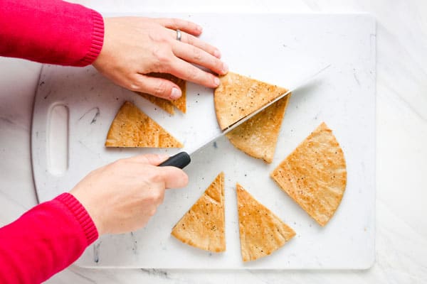 Overhead view of cutting seasoned pita bread into wedges with a knife.