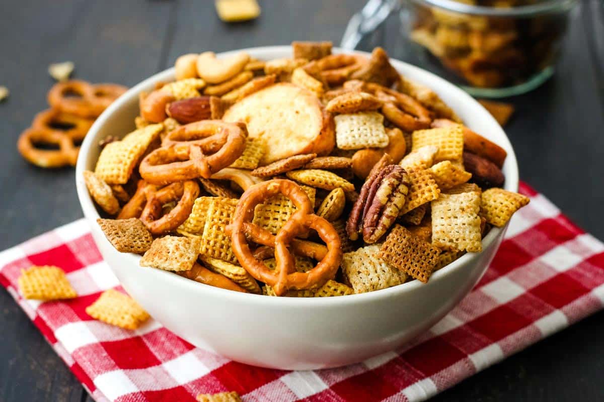 Bowl of snack mix on red checkered napkin.