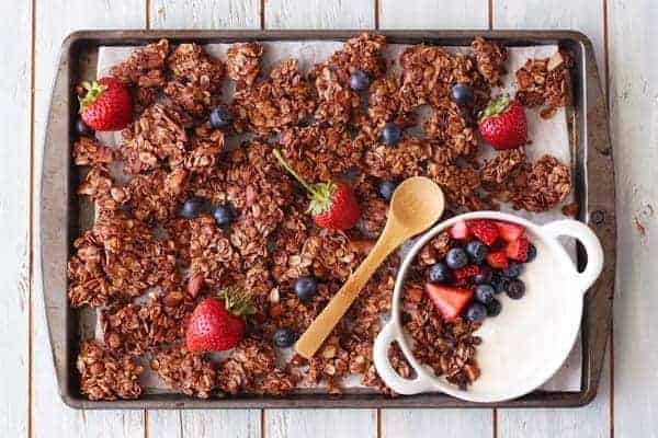 Chocolate granola on a baking sheet with fresh berries.