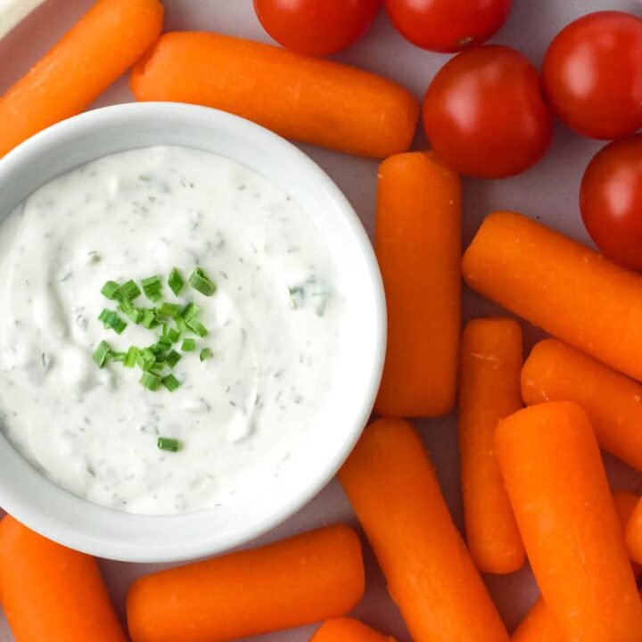 Plate with baby carrots, cherry tomatoes, and ramekin of ranch dip.
