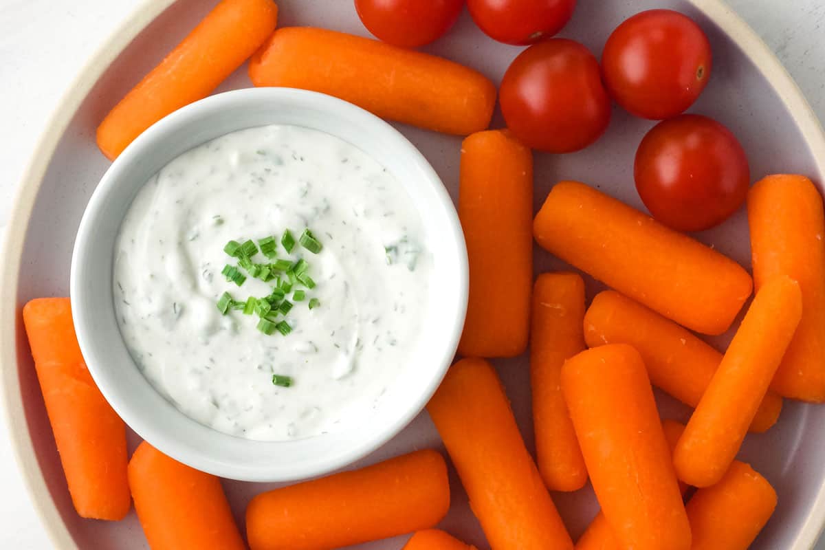 Plate with baby carrots, cherry tomatoes, and ramekin of ranch dip.