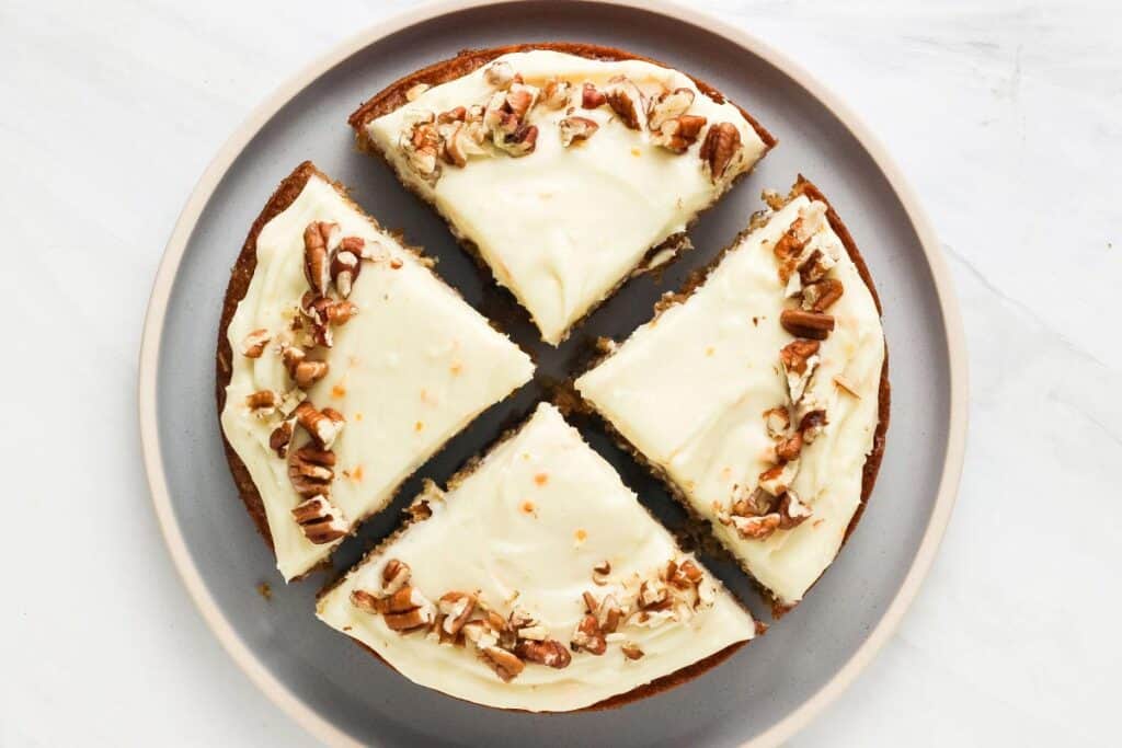 Overhead view of frosted cake topped with chopped pecans and cut into four slices.