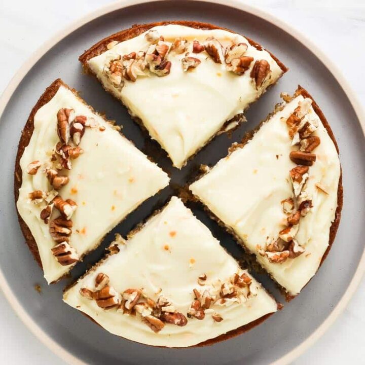 Overhead view of frosted cake topped with chopped pecans and cut into four slices.