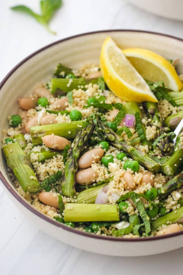 Closeup of roasted asparagus, peas, and couscous in a tan bowl.