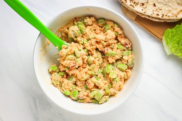 Bowl of prepared chickpea edamame salad next to pita bread and lettuce.