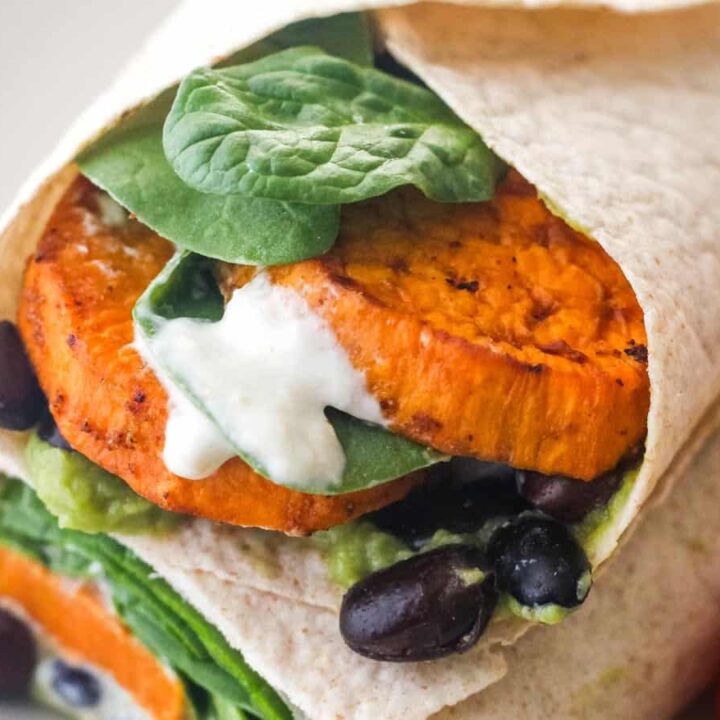 Closeup of sweet potato slices, black beans, and sauce in a wrap.