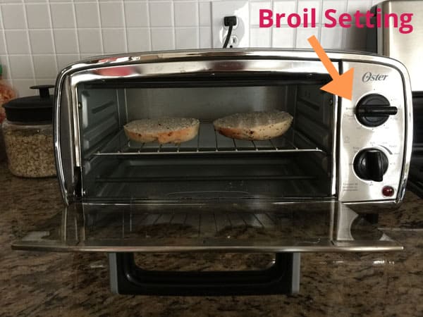 Small toaster oven with bagel slices inside and an arrow pointing to the Broil setting.