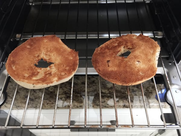 Toasted bagel slices on a toaster oven cooking rack.