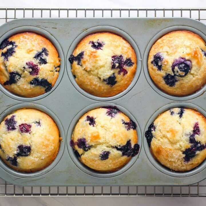 Six muffins with golden brown tops and bursting with juicy blueberries.