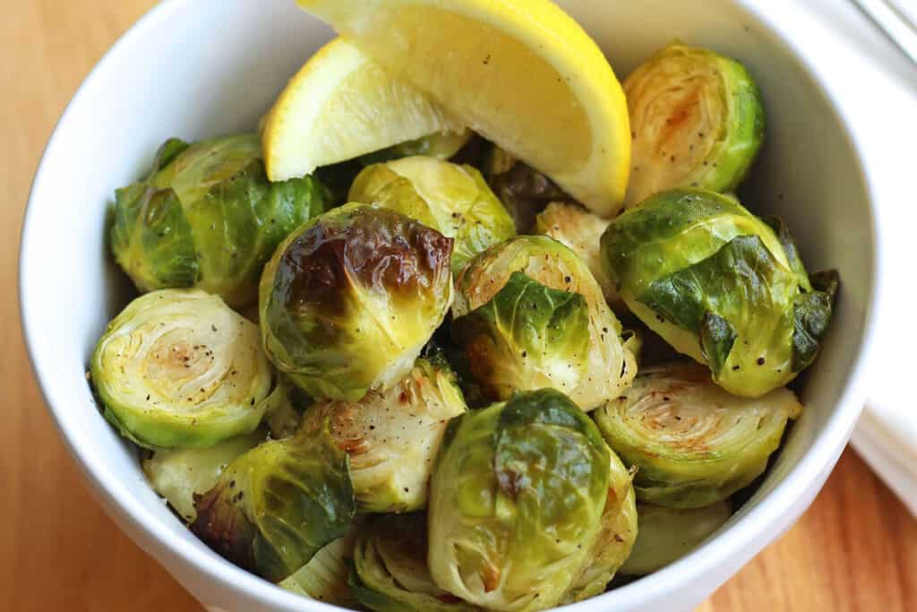 Closeup of cooked Brussels sprouts with lemon wedges in a bowl.