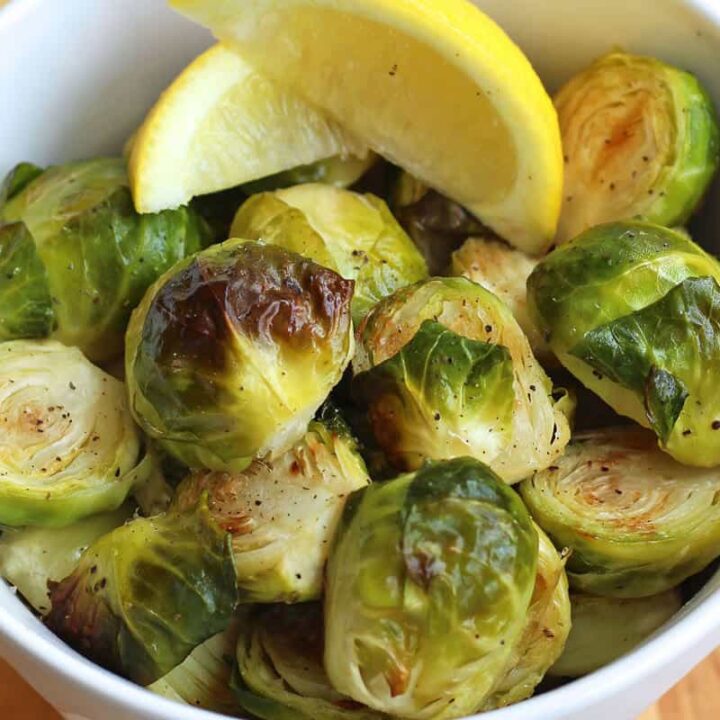 Closeup of cooked Brussels sprouts with lemon wedges in a bowl.
