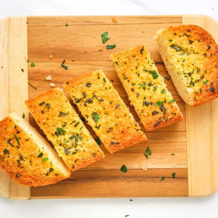 Garlic bread roll sliced into pieces on a cutting board.