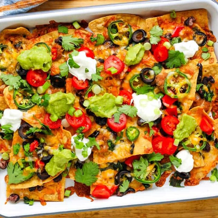 Pan of baked nachos topped with guacamole, tomatoes, green onions, and dollops of yogurt.