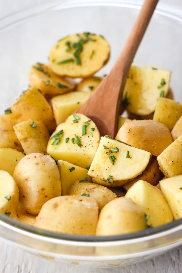 A glass bowl filled with chopped baby potatoes and fresh rosemary with a wooden spoon.