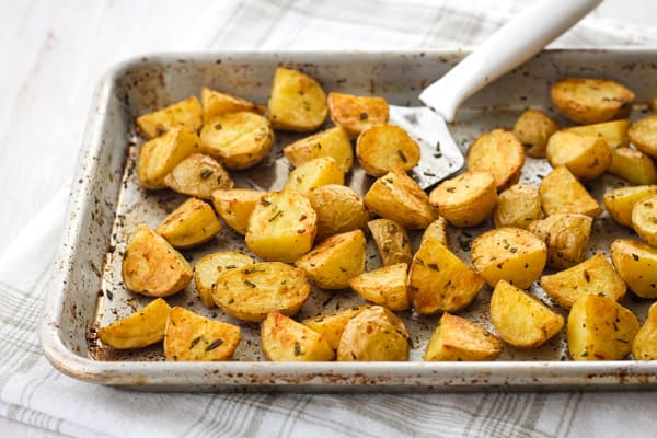 Cooked potatoes on a quarter sheet pan with a metal spatula.