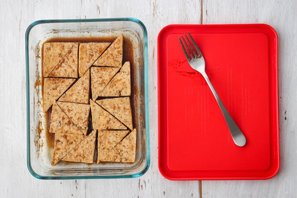 Sliced tofu marinading in a glass dish with a lid next to it.