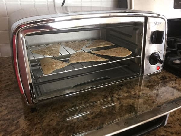 Flour tortilla slices baking on a toaster oven cooking rack.