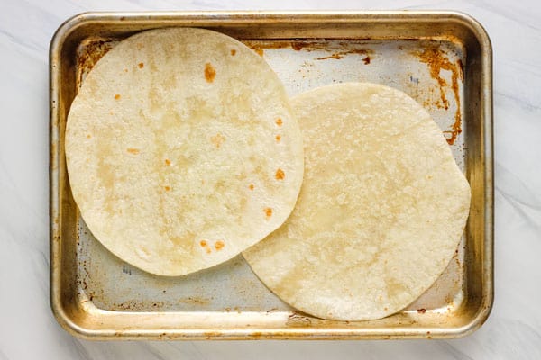 Oiled tortillas slightly overlapping on a quarter sheet pan.