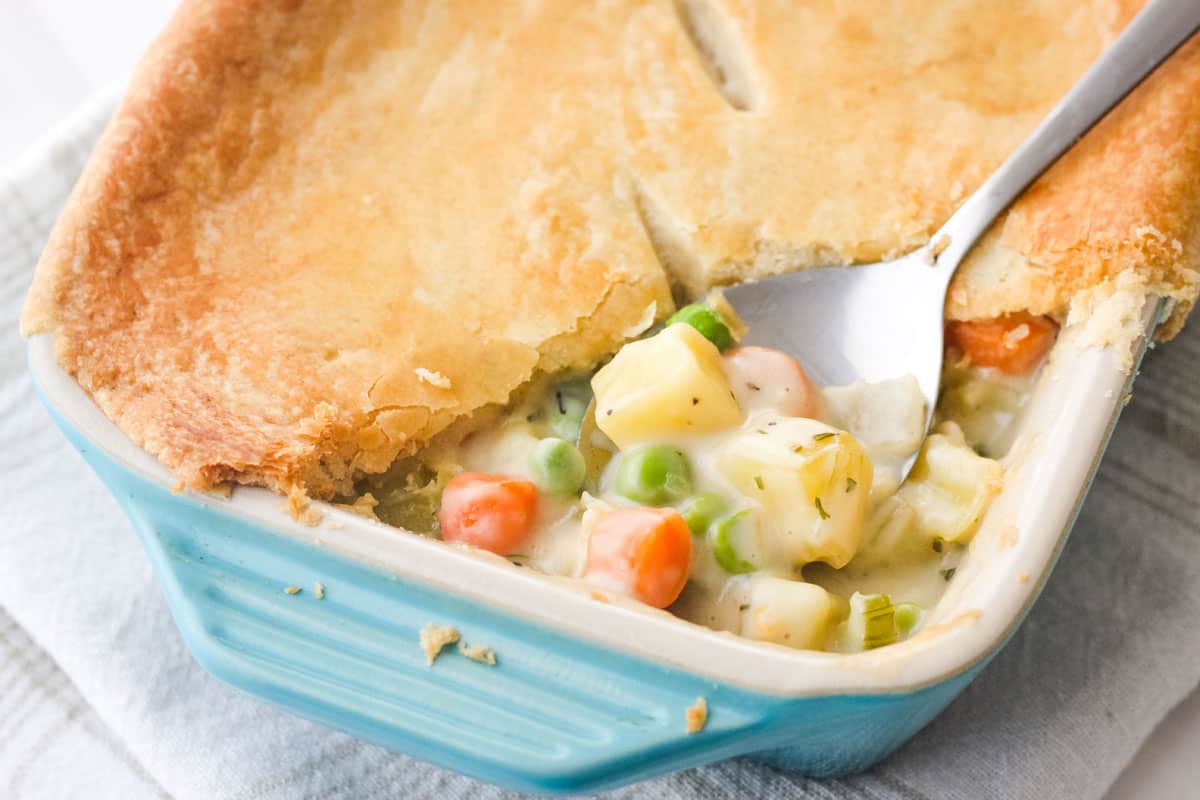 Closeup of spoon scooping creamy vegetable pot pie filling and crust from a small baking dish.