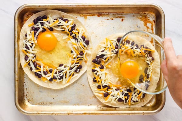 Hand pouring bowl of egg in center of tortilla on a pan.